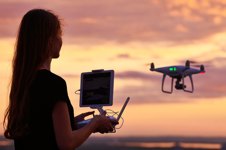 drone quadcopter with digital camera operated by woman at sunset