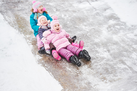 children having fun riding ice slide in winterの写真素材