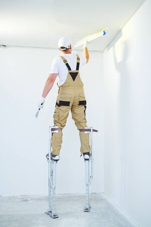 Painter in stilts with putty knife. Plasterer smoothing ceiling surface at home renewalの写真素材