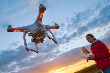 drone flying at sunset piloted by young womanの写真素材