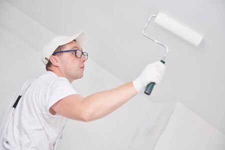 Painter worker with roller painting ceiling surface into whiteの写真素材