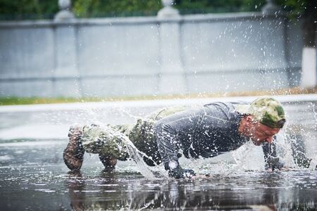 Man in military clothing training outdoors. Doing push ups in on drill square. Focus on splashesの写真素材