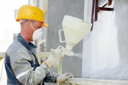 construction worker painter spraying paint onto otside wall surface of building facadeの写真素材
