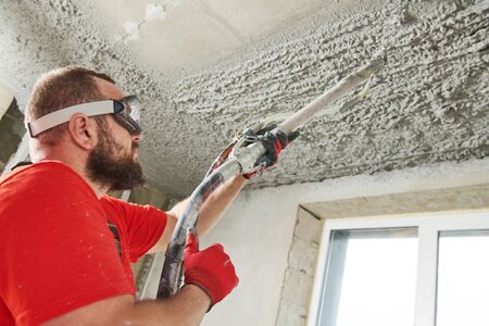 Plasterer using sprayer machine putting plaster mortar on ceilingの写真素材