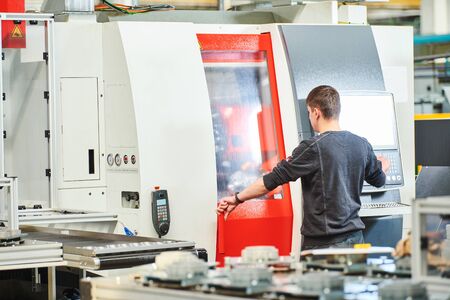Industrial worker or service engineer operating cnc milling lather machine at factory in metal...