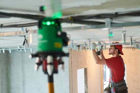 Gypsum plasterboard work. Drywall construction at home. Contractor worker installing metal frame on ceilingの写真素材