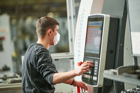 Industrial worker operating cnc machine in protective mask at metal machining industry