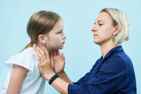Pedeatrician female doctor making throat palpation of little girlの写真素材