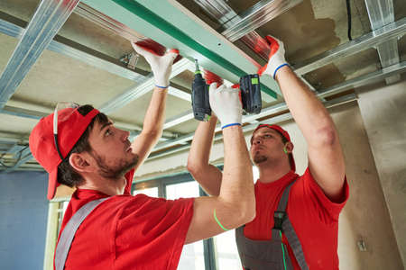 Plasterboard Ceiling Installation. Two workers installing gypsum drywall