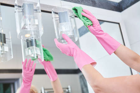 Woman cleaning and wiping glass lamp in bathroom with wiper cloth in bathroomの写真素材