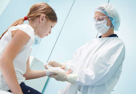 female surgeon doctor, in focus, bandaging childs hand in clinic