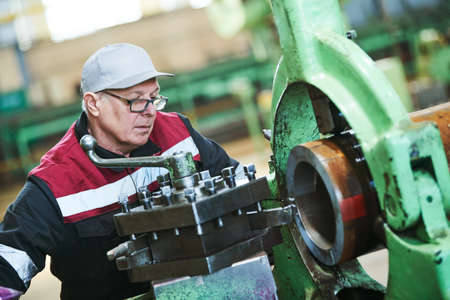 worker turner operating lathe machine at industrial manufacturing factory