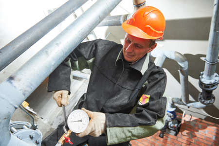 Plumber technician works with water pressure meter in boiler roomの写真素材