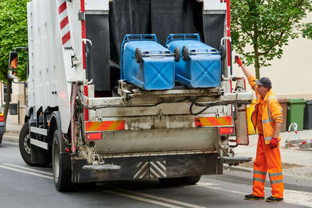 garbage and waste removal services. Worker loading waste bin into truck at cityの写真素材