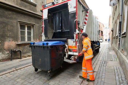 garbage and waste removal services. Worker loading waste bin into truck at cityの写真素材