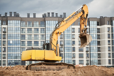 construction machine excavator standing in front of modern apartment building. Real estate developmentの写真素材