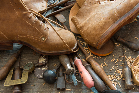 Old shoemaker tools with handmade shoes on workshop bench.の写真素材