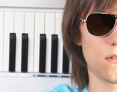 Portrait of young man in sunglasses with piano, isolated on white backgroundの写真素材