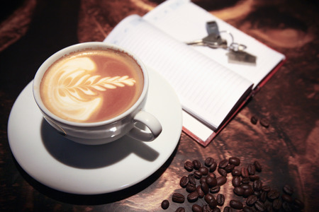 Cup of coffee on the desk  and  house keys on notebookの写真素材