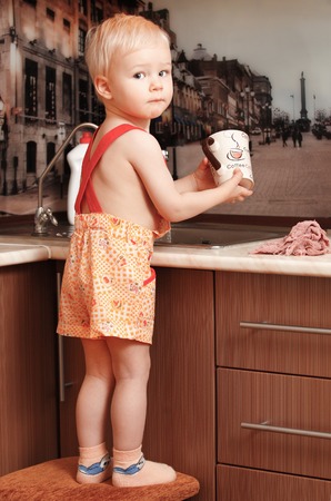 Portrait of a child holding a cup at the kitchen at homeの写真素材