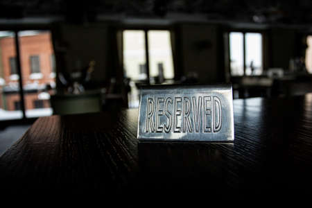 Metal plaque Reserved on the black table in a cafe against a background of blur and light in the...