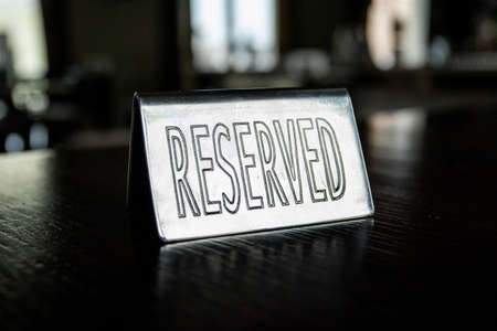 Metal plaque Reserved on the black table in a cafe against a background of blur and light in the windows. High quality photoの素材 [FY310168661752]