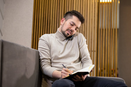 Young bearded man writes in a diary while working from home. Remote job.
