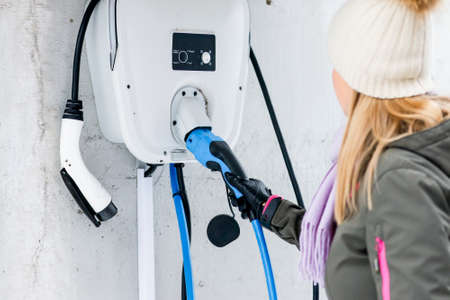 charging station, ecological fuel concept. Portrait of a beautiful young girl holding the charging plug in her modern electric car for refueling at a city station.の写真素材