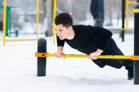 Young man doing morning exercises, doing fitness outdoors in winter in the snow with the help of the yellow exercise machine.の写真素材