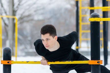 Young man doing morning exercises, doing fitness outdoors in winter in the snow with the help of the...