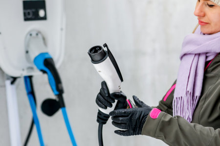 charging station, ecological fuel concept. Portrait of a beautiful young girl holding the charging plug in her modern electric car for refueling at a city station.の写真素材