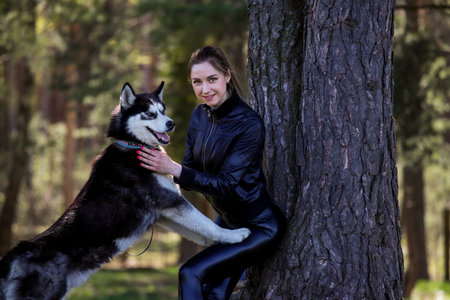 An attractive girl plays with a husky in the forest in a clearing.の写真素材