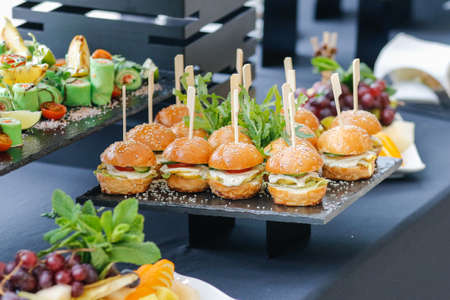 A set of several burgers for catering. Burgers on a black plate on the buffet table.