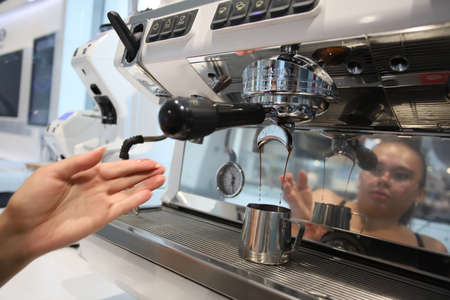 Minsk. Belarus - 06.06.2021: A cute barista makes coffee in a coffee machine.のeditorial素材