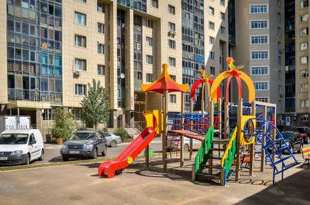 Nur-Sultan. Kazakhstan: 04.09.2013 - Childrens playground in a yellow residential building, a residential complex against a blue sky. Kazakhstan.のeditorial素材