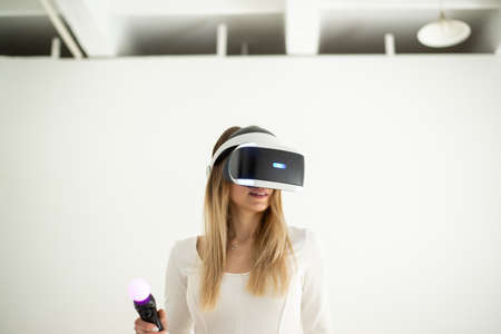 Beautiful blonde in virtual reality glasses with the remote control in her handsの写真素材