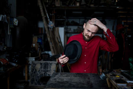 A man in a red shirt and hat scratches his bald headの写真素材
