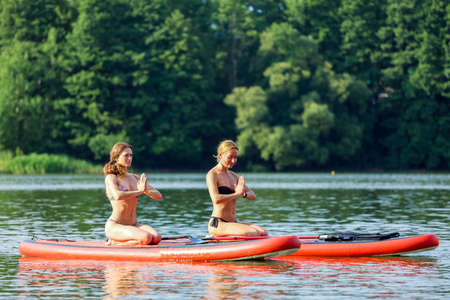 Two young women doing yoga together on the board in a middle of the lake. High quality photoの写真素材