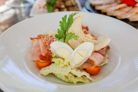 Egg, croutons, tomato, ham salad in a white plate on a table. High quality photoの写真素材