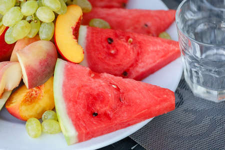 Red watermelon, peach, grapes on a white plate on a table. High quality photoの写真素材