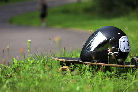 A helmet on the longboard in black with a sticker number 13 lies in the grass. High quality photo