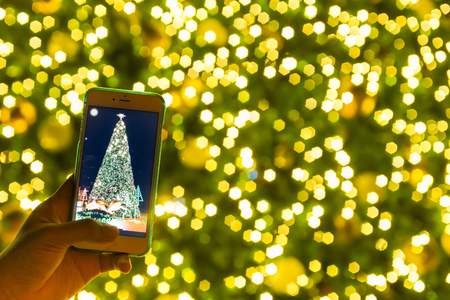 blurred christmas tree replay on screen of smart phone with bokeh backgroundの写真素材