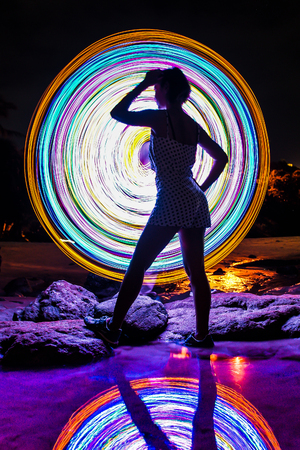 light lines of flashlight with long exposure and blur sexy silhouette posting lady  with reflection in water, speed motion abstract background in the dark nightの写真素材