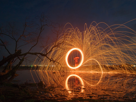 light lines of steel wool with long exposure, speed motion abstract background in the dark night with dry branch tree and reflection in water,look like dick penisの写真素材