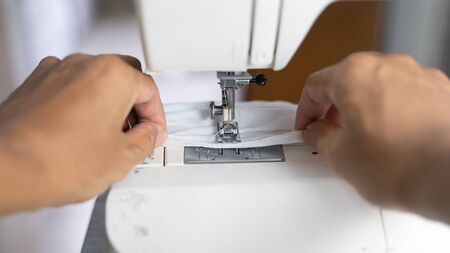 Electric sewing machine with fabric and thread, defocus hand hold on protective mask , antivirus ...