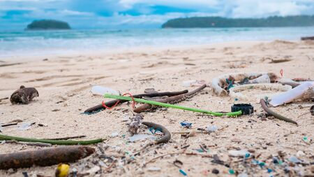 Environmental pollution. Ecological problem. Garbages, plastic, and wastes on the sandy beach of tropical sea. Island and mountain background.の写真素材