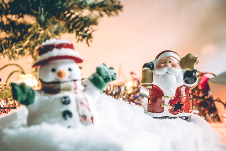Snowman and Santa claus hold bell among pile of snow at silent night with a light bulb, light up the hopefulness and happiness in Merry christmas and new year night.の写真素材