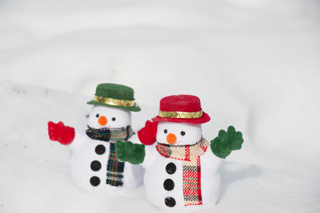 Snowman and friend stand among pile of snow in park. Morning sunshine is warming in winter. Welcome christmas season.の写真素材