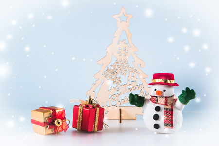 Snowman and  gift box stand near christmas tree on white background. Snow flake is falling down.の写真素材