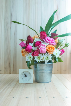 Vase of bouquet Roses in aluminium bucket and white clock on wooden table, set of Beautiful flowerの写真素材
